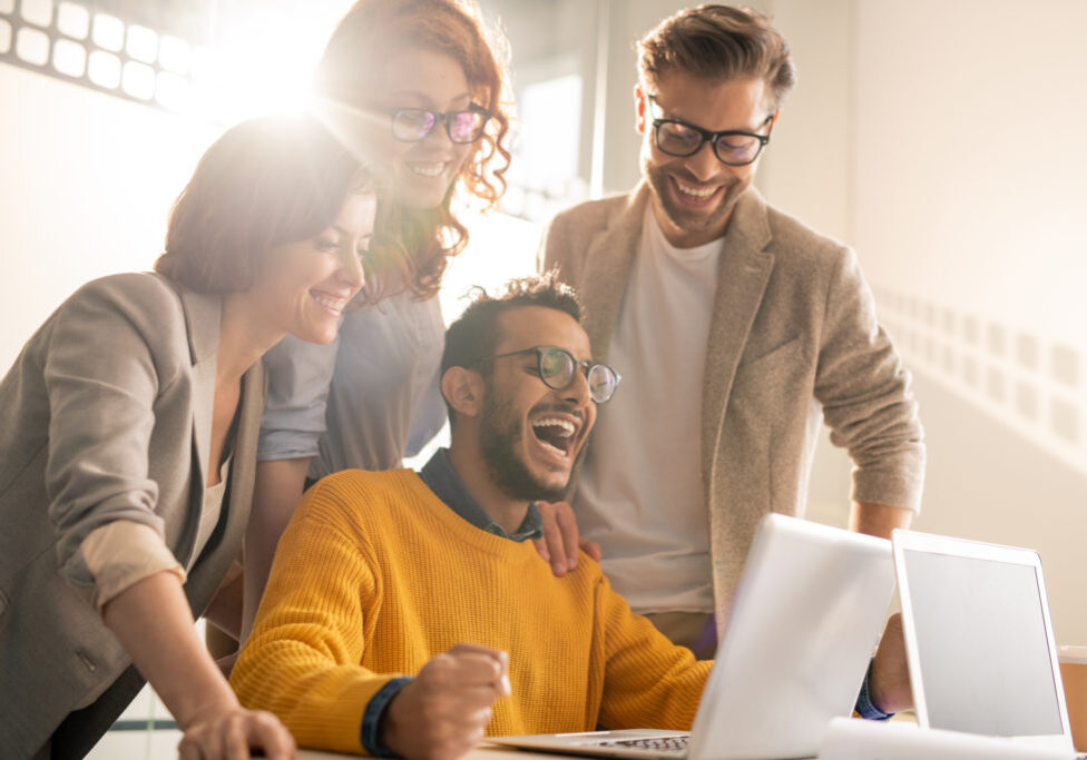 Excited colleagues reading internet news Group of cheerful excited young interracial colleagues laughing while reading internet news on laptop